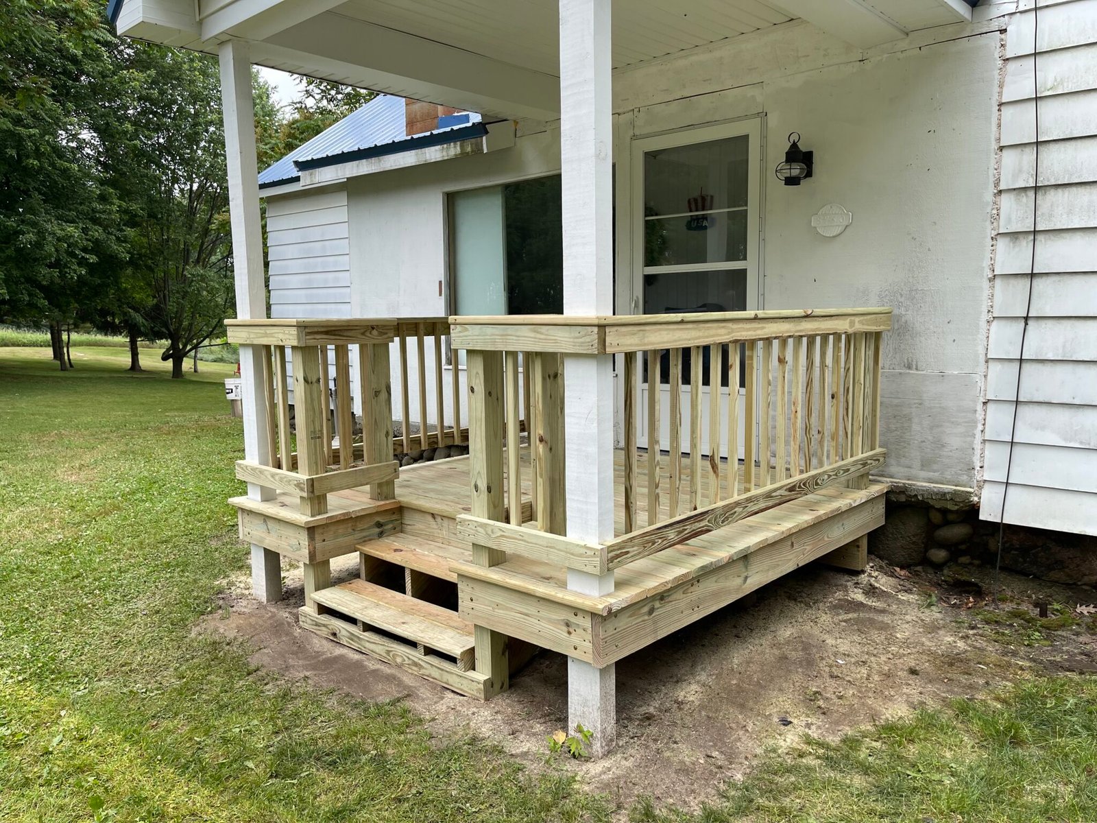 Covered front porch with white railing and wood decking on a farmhouse-style home