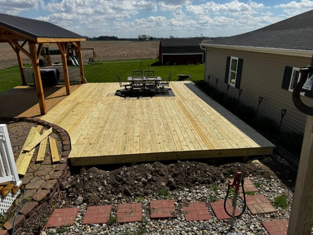 New unstained wood deck with pergola frame overlooking a rural backyard