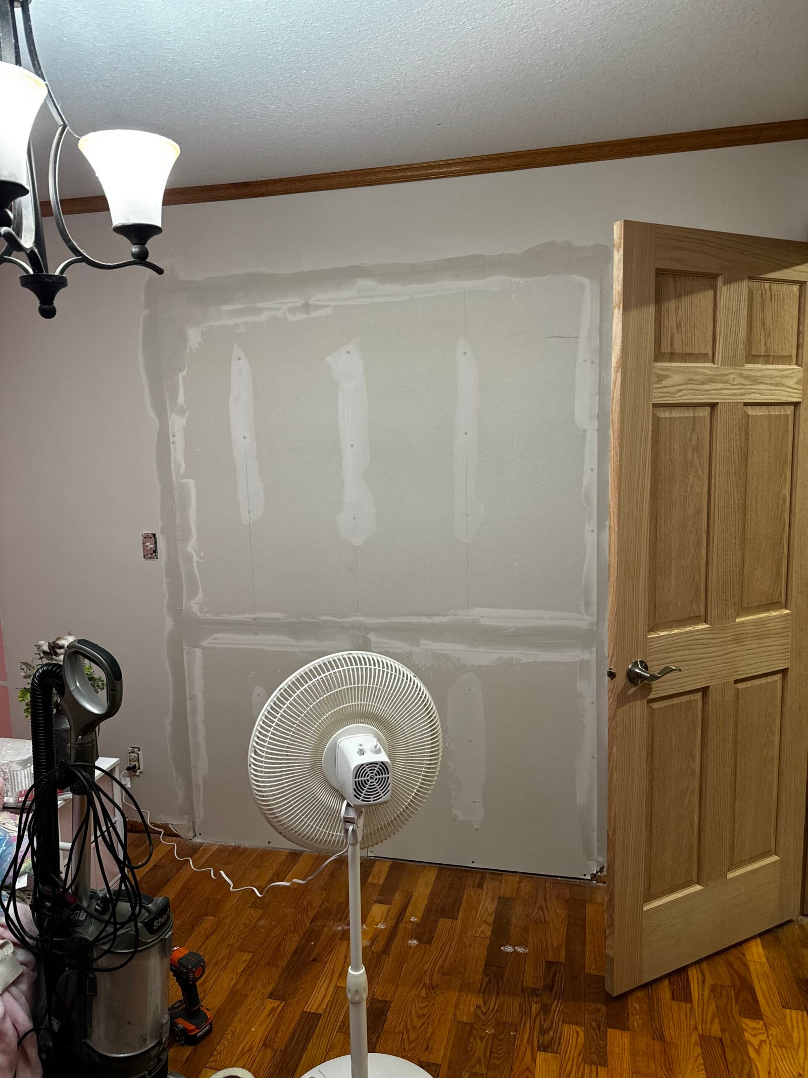 Drywall patch and repair work in progress in a living room with hardwood floors