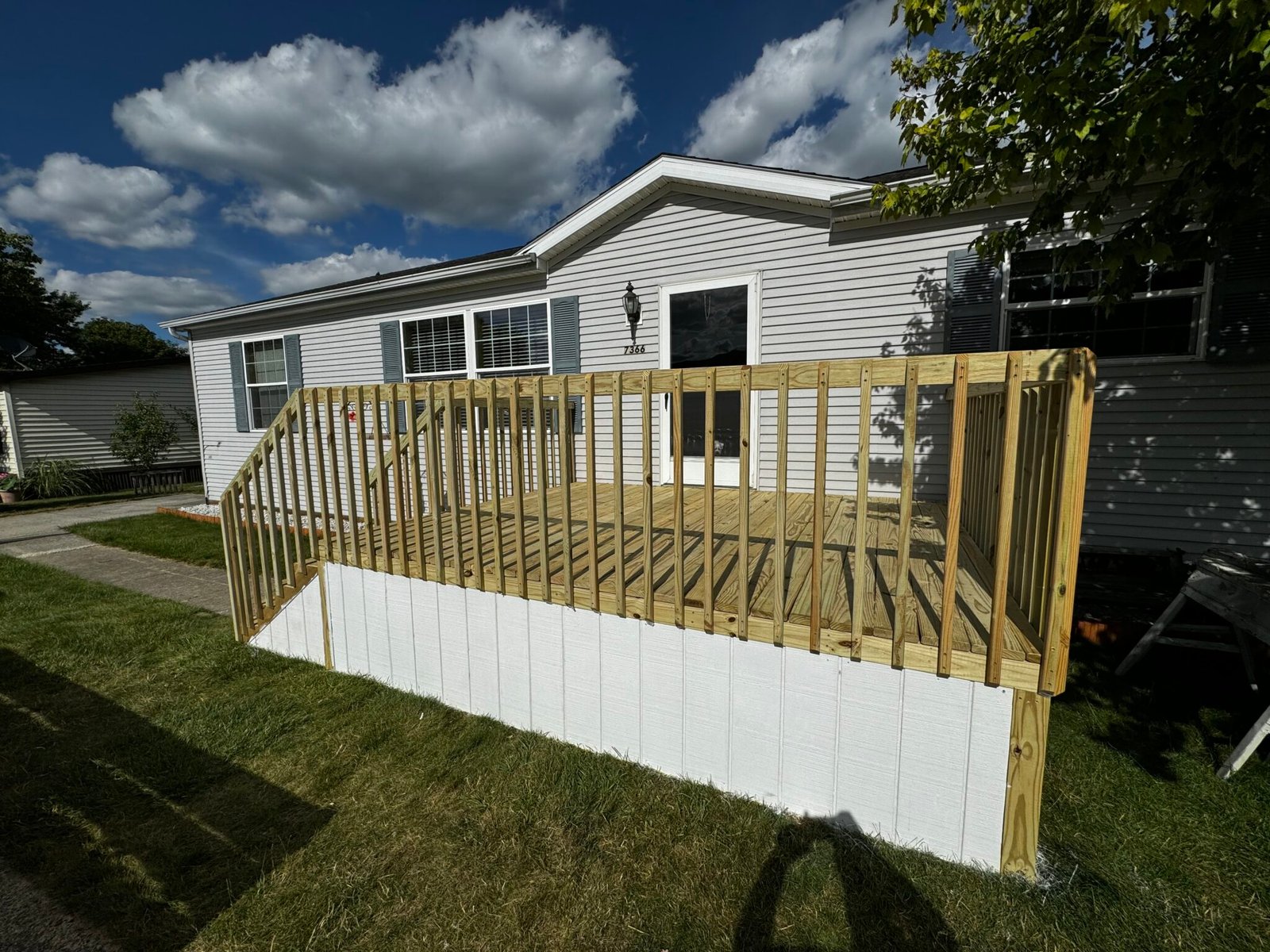New wood deck with white vinyl railing along the side of a manufactured home