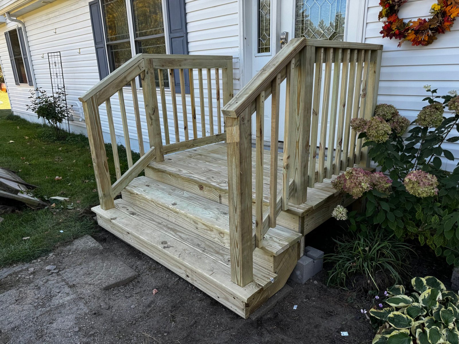 New wood deck steps with white railing next to a landscaped flower bed