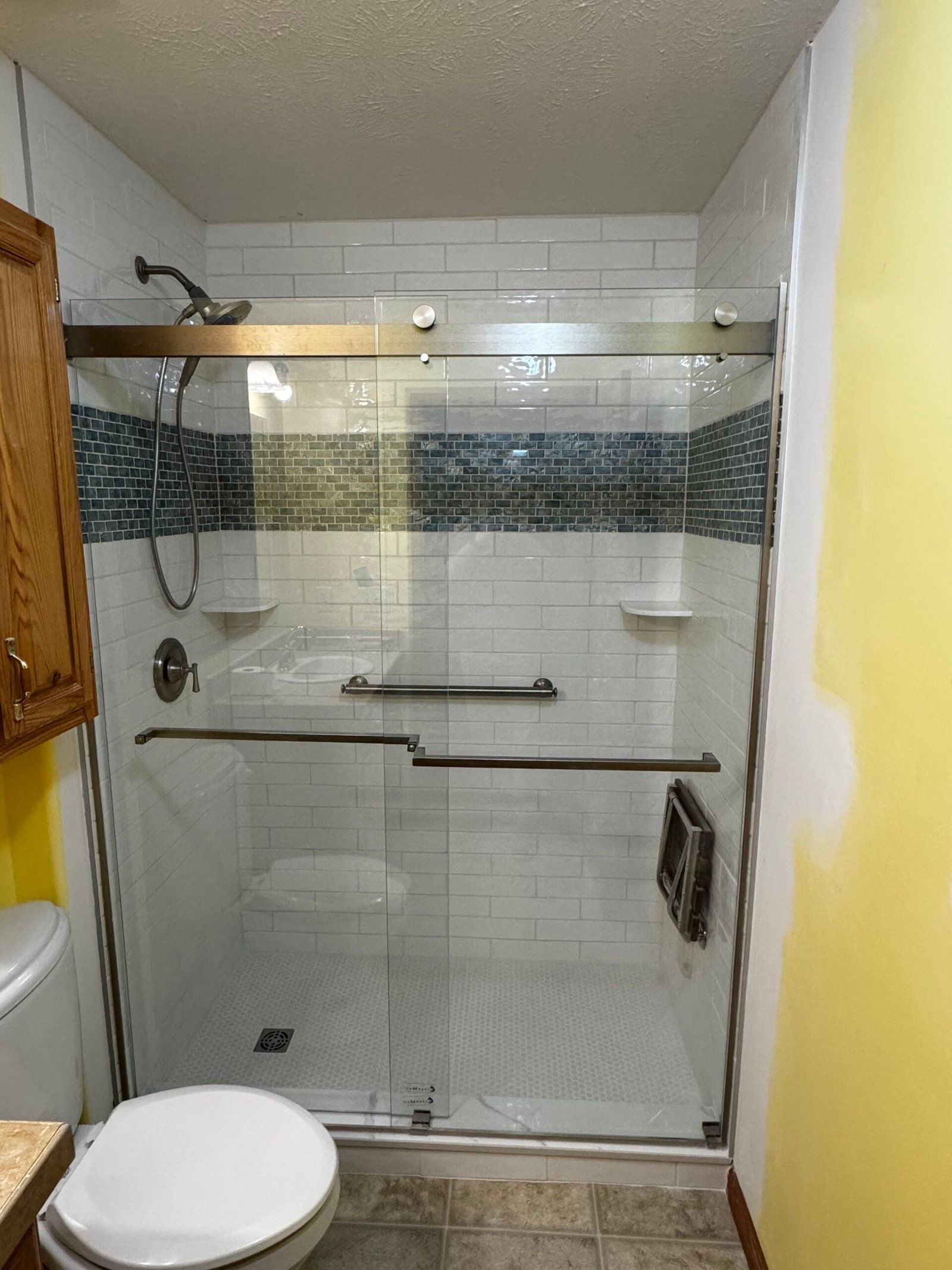 Remodeled bathroom with sliding glass shower enclosure and tile accent band