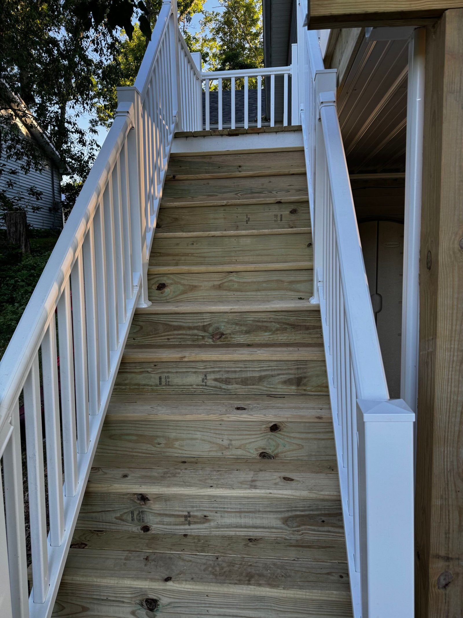 Exterior wood staircase with white vinyl railing leading to a side entry