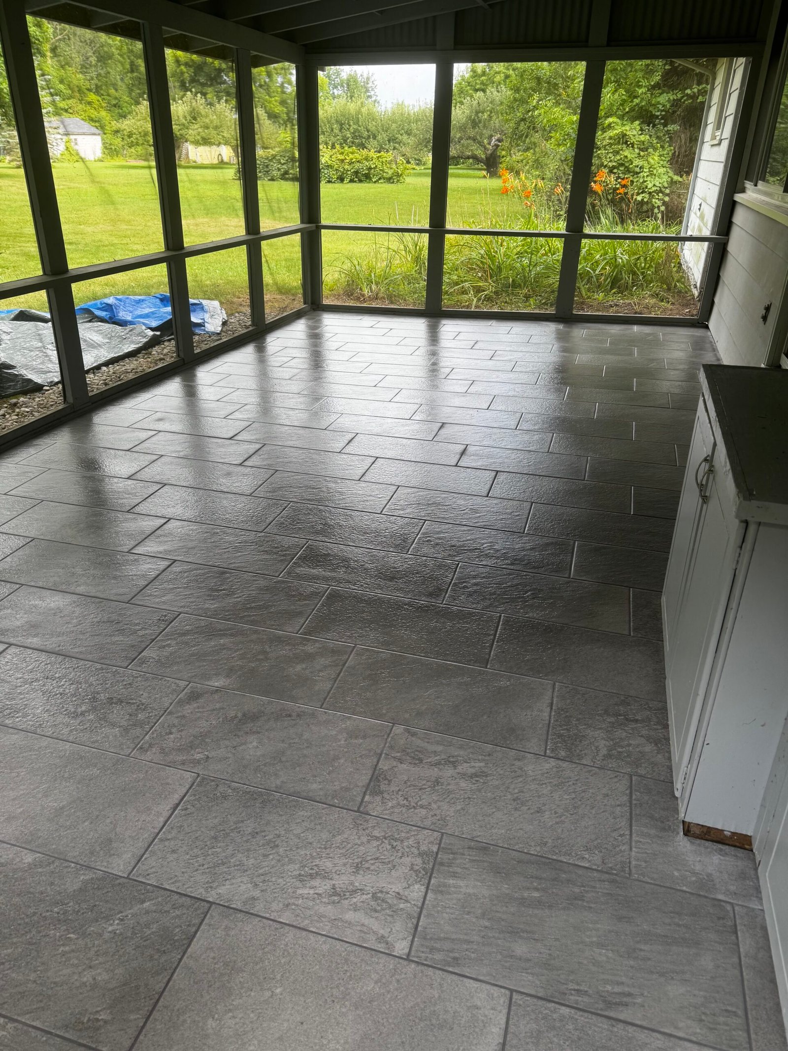 Screened three-season porch with tile flooring and green yard view