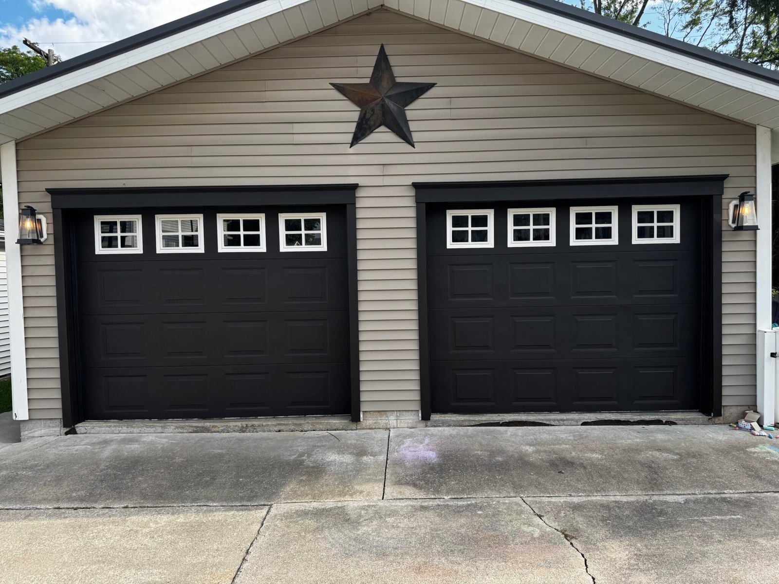 Two-car garage with new black garage doors on a tan-sided home