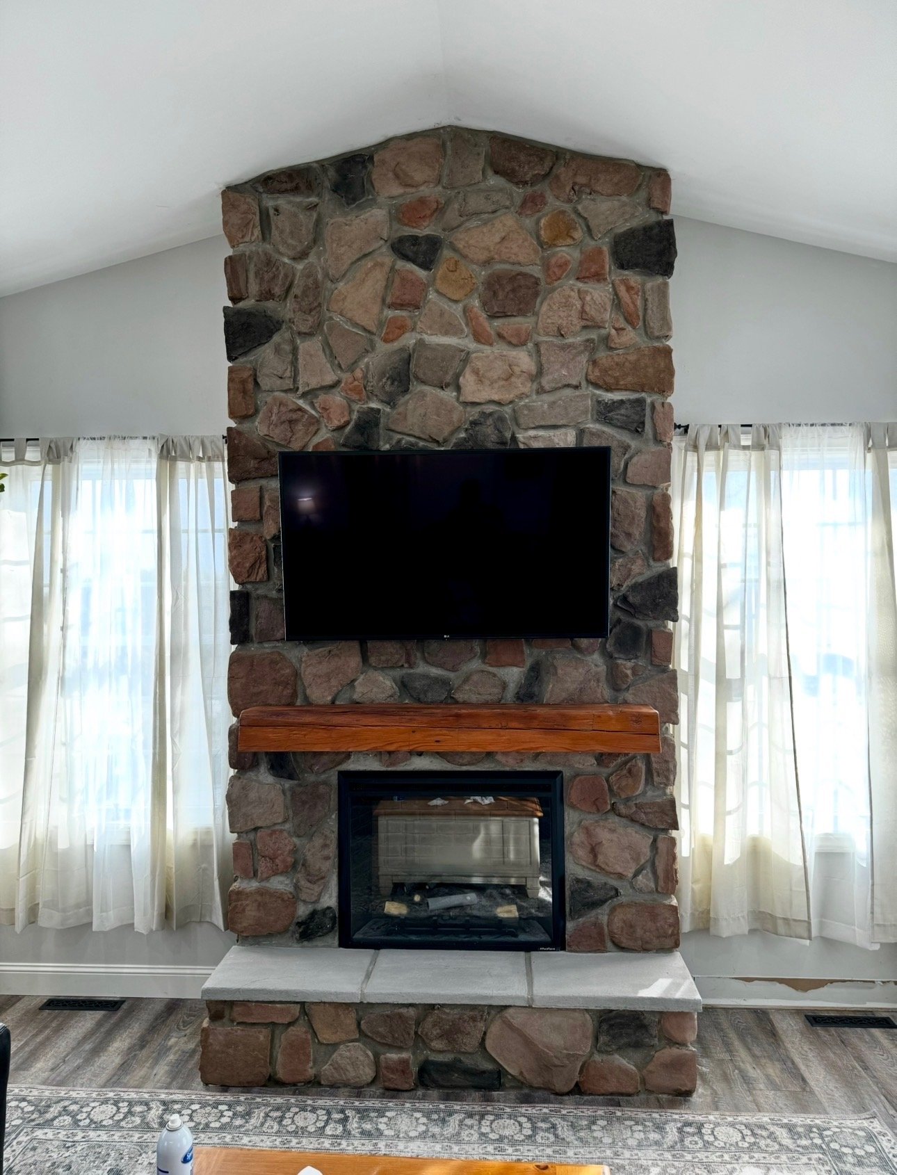 Stone veneer fireplace surround with wood mantel and wall-mounted TV