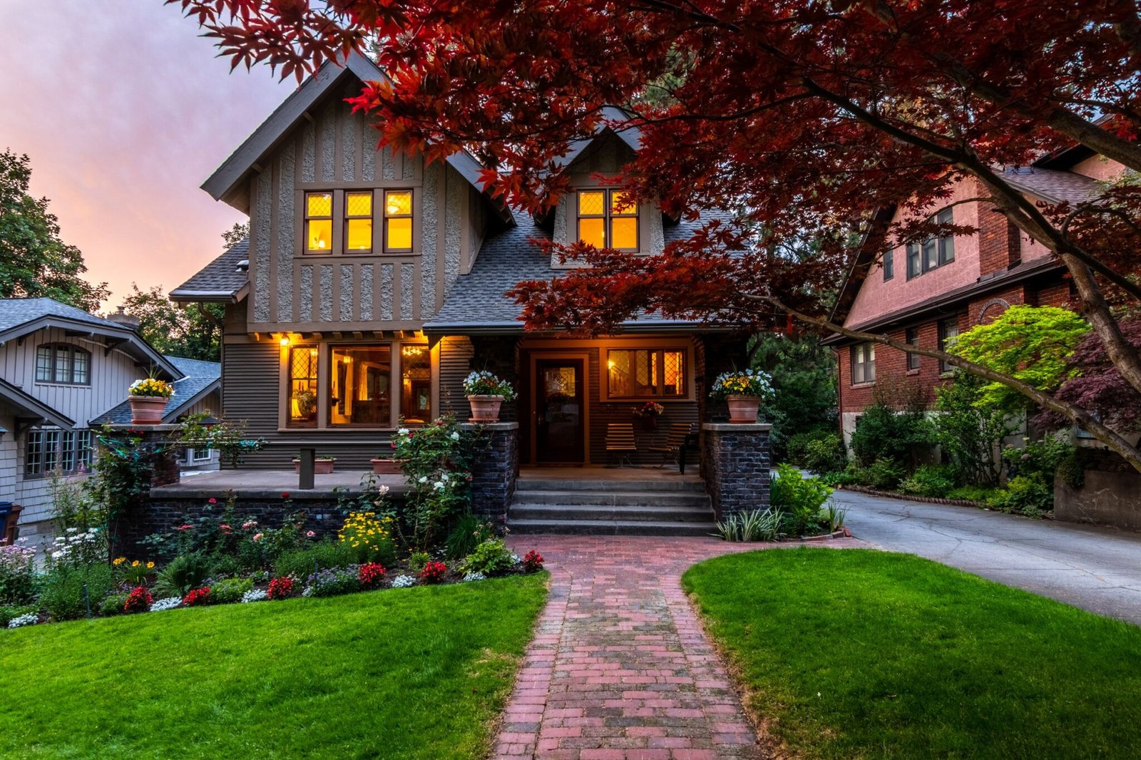 Craftsman-style home at dusk with warm lit windows, a brick front walk and a red maple